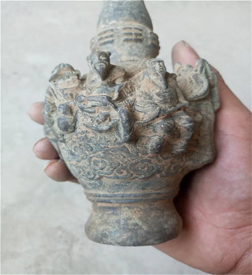 Hand holding a stone sculpture of a figure with multiple heads and arms on a plain background