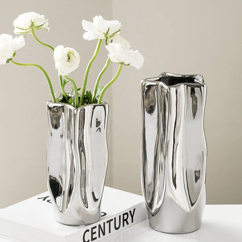 Two silver vases with white flowers on a light surface.