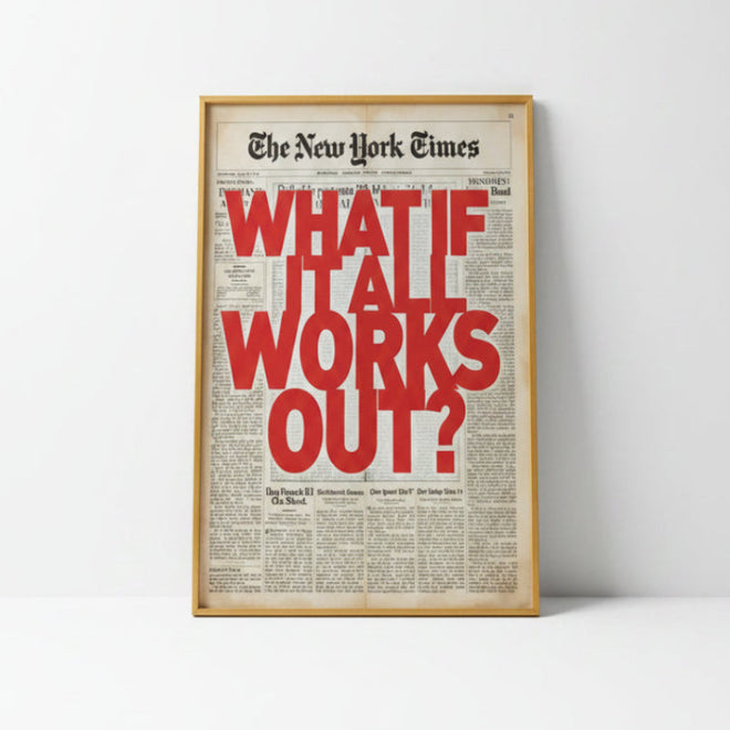 A framed New York Times newspaper-style wall art print leaning against a wall on a wooden floor, with large red text reading “WHAT IF IT ALL WORKS OUT?” on an off-white newspaper background. A white chair is partially visible at the right, and sunlight streams in from a window on the left.