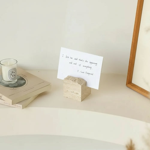 Wooden photo holder with a card on a surface with a candle and books.