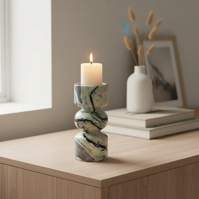 Marble-patterned candle holder with a lit candle on a wooden surface, with a vase and photo frame in the background.