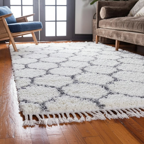 White geometric patterned rug with fringe on a wooden floor in a living room.