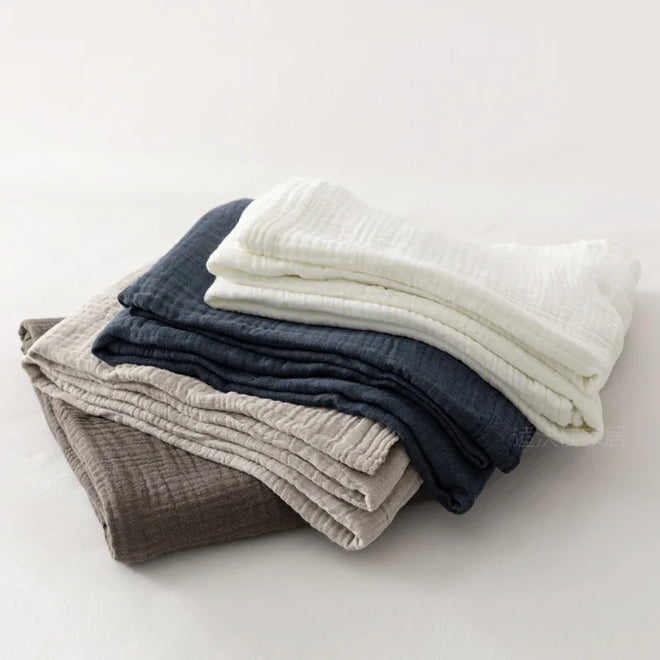 Dark blue washed organic triple-layer cotton gauze throw blanket from The Finishing Touch Decor, 140x200cm, draped over a cozy chair.